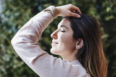 Beautiful woman with hand in hair at balcony on sunny day - EBBF02922