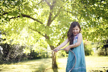 Smiling girl watering through hose in garden - BRF01490