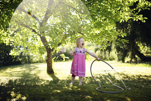 Cute cheerful girl enjoying while watering grass with garden hose - BRF01491