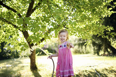 Glückliches Mädchen gestikuliert, während sie ein Bewässerungsrohr im Garten hält - BRF01492