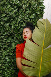 Woman holding green banana leaf while standing in front of plants - TCEF01730