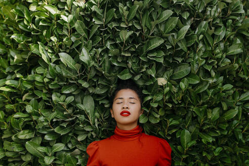 Woman with eyes closed in front of green plants - TCEF01733