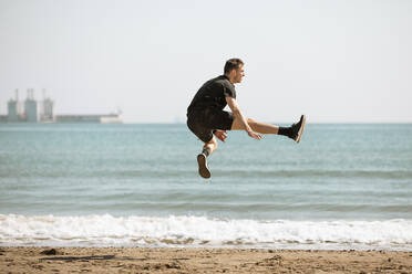 Young man jumping while exercising on sunny day - ACPF01204