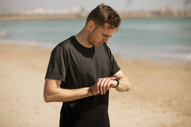 Junger Mann prüft am Strand die Zeit auf seiner Armbanduhr - ACPF01205
