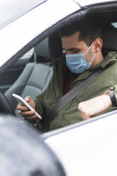 Man with protective face mask using mobile phone while sitting in car - JAQF00442