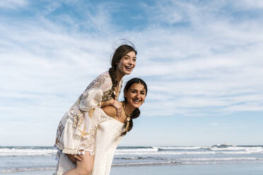 Verspielte Frau nimmt ihre Freundin am Strand huckepack - EGAF02200