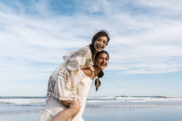 Carefree woman enjoying while piggybacking with friend at beach - EGAF02201