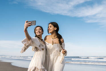 Young smiling woman taking selfie with friend through mobile phone during sunny day - EGAF02203