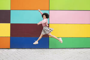 Carefree young woman jumping with arms outstretched on footpath - JCCMF01561
