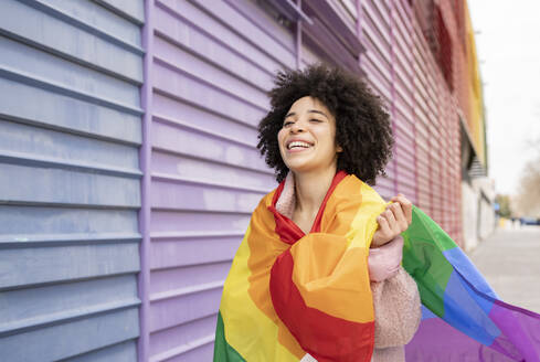 Cheerful woman wrapped in rainbow flag - JCCMF01597