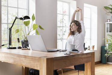 Weibliche Unternehmerin streckt die Hände am Schreibtisch im Heimbüro aus - SBOF03596