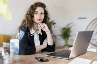 Thoughtful female entrepreneur looking away while holding eyeglasses at desk - SBOF03611