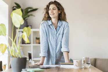 Happy female professional leaning at desk in home office - SBOF03639