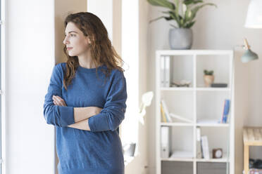 Thoughtful woman with brown hair looking away while standing in living room at home - SBOF03659
