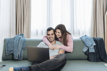 Lächelndes erwachsenes Paar, das im Hotel auf einen Laptop schaut - DGOF02051