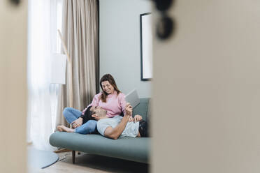 Smiling woman looking at man lying on lap in hotel room - DGOF02053