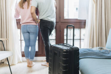 Gepäck mit einem Paar, das im Hintergrund am Fenster eines Hotelzimmers steht - DGOF02054