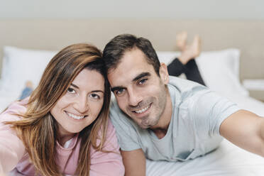 Smiling couple lying together on bed in hotel room - DGOF02067