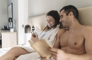 Woman using mobile phone while sitting by man in hotel room - DGOF02086