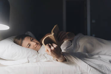 Frau liest ein Buch, während sie auf dem Bett im Hotelzimmer liegt - DGOF02091