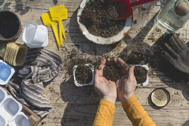 Woman holding soil over container on table in garden - SKCF00731