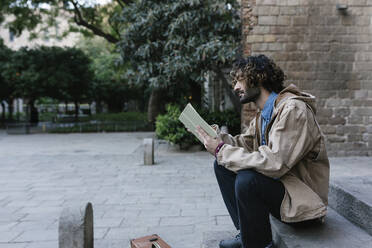 Junger Mann liest ein Buch, während er auf einer Treppe sitzt - XLGF01382