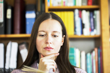 Thoughtful woman with hand on chin reading book at home - SGF02799