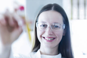 Lächelnde Wissenschaftlerin mit Reagenzglas im Labor - SGF02802
