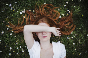 Redhead woman covering eyes while lying on grass - EBBF02923