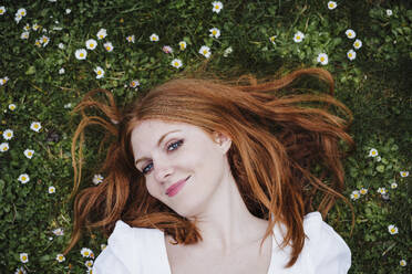 Smiling redhead woman lying on grass - EBBF02927