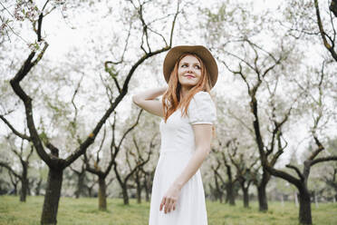 Smiling woman standing in park while looking away - EBBF02956