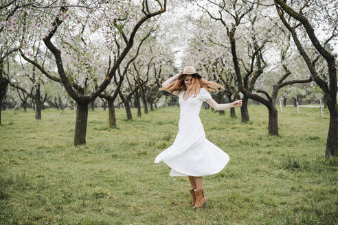 Glückliche junge Frau tanzt unter einem Baum im Park - EBBF02959