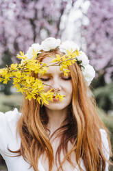 Rothaarige Frau mit geschlossenen Augen, die ein Blumen-Diadem trägt und einen Strauß gelber Blumen hält - EBBF02966