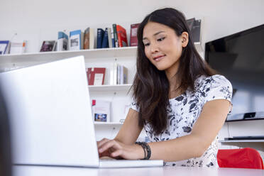 Junge Frau arbeitet am Laptop in einer Bibliothek - BMOF00525