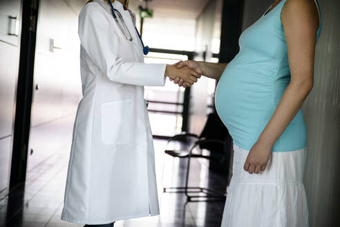 Female doctor shaking hands with pregnant woman after examining at hospital - BMOF00530