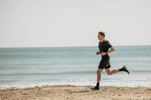 Junger Mann läuft am Strand während eines sonnigen Tages - ACPF01206