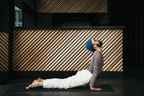 Male fitness instructor practicing cobra pose in exercise room - MJRF00365