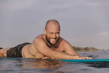 Lächelnder männlicher Surfer auf einem Surfbrett an einem sonnigen Tag - KNTF06205