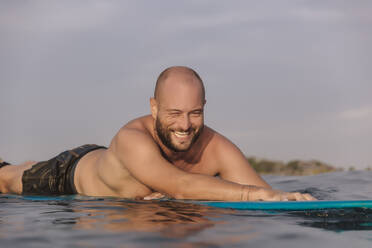 Smiling male surfer floating on surfboard during sunny day - KNTF06205