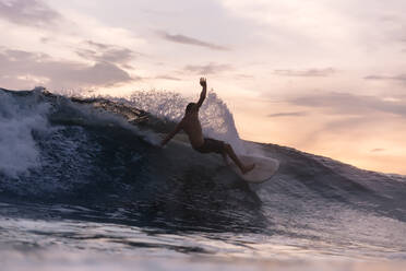 Tourist surfing over waves in sea during sunset - KNTF06206