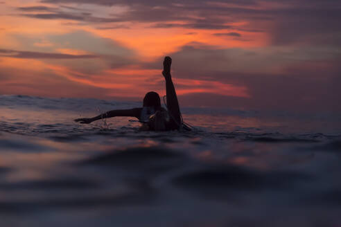 Frau schwimmt auf Surfbrett im Meer bei Sonnenuntergang - KNTF06208