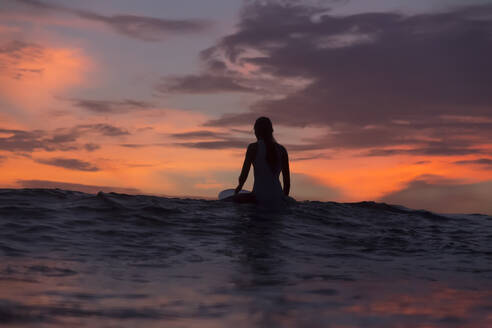 Weibliche Surferin auf Surfbrett im Meer sitzend im Urlaub - KNTF06209