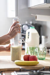 Frau bereitet Fruchtmilchshake mit elektrischem Mixer zu Hause zu - WPEF04233