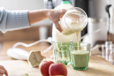 Frau gießt Smoothie in Glas auf Küchentisch - WPEF04234