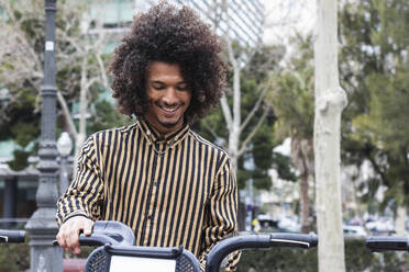 Smiling young man with curly hair sitting on bicycle - PNAF01256
