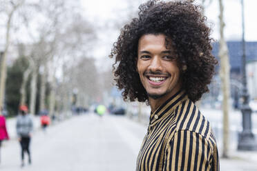 Young man with curly hair looking away on footpath - PNAF01260