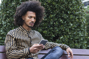 Young man using mobile phone on bench - PNAF01264