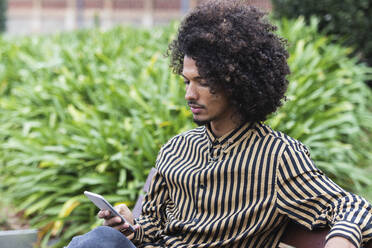 Junger Mann benutzt Mobiltelefon in einem öffentlichen Park - PNAF01287