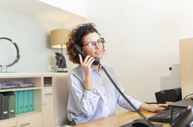 Receptionist talking on telephone at desk in hotel - JPTF00716