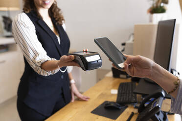 Geschäftsfrau hält Mobiltelefon an Kreditkartenleser an der Hotelrezeption - JPTF00726